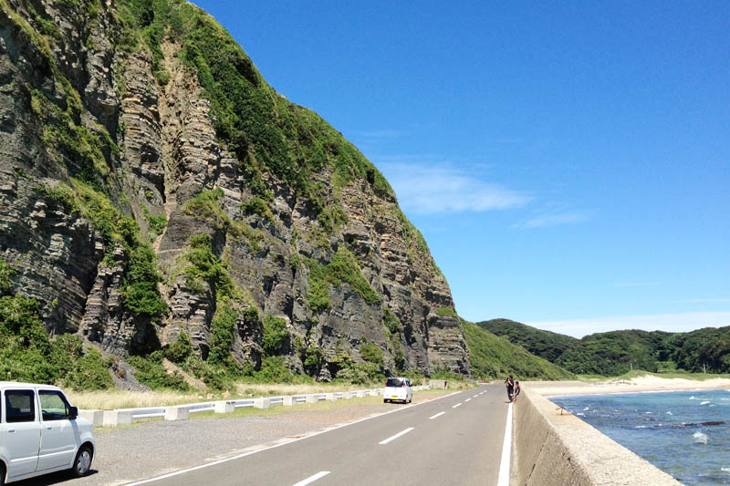 真ん中に道路が走り、左側に壱岐の土台石と呼ばれる絶壁があります。頁岩と砂岩からなる堆積層が何層にも重なっています。道路の右側は海岸です。