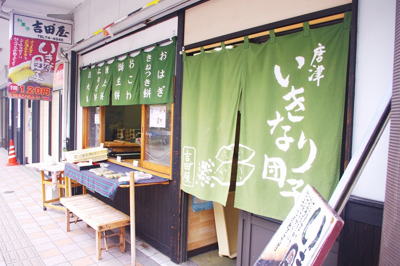 This is the exterior of a Japanese sweets shop in Karatsu called Yoshida-ya, famous for its Ikinari-dango. The entrance and windows of the store are covered with green curtain.