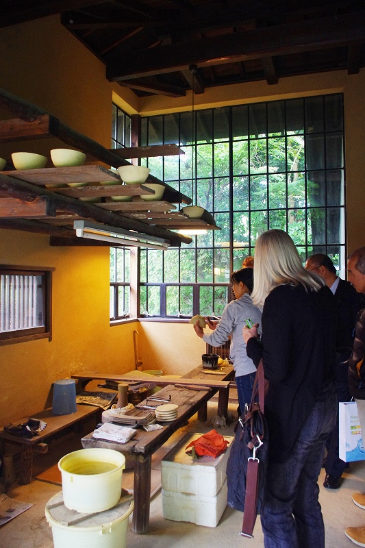 This is the inside of the workshop of Nakazato Taroemon of Karatsu ware. The room has a high ceiling and large windows, and the shelves are filled with pottery that has been made. Some visitors from overseas are listening to the explanation from the craftsman.