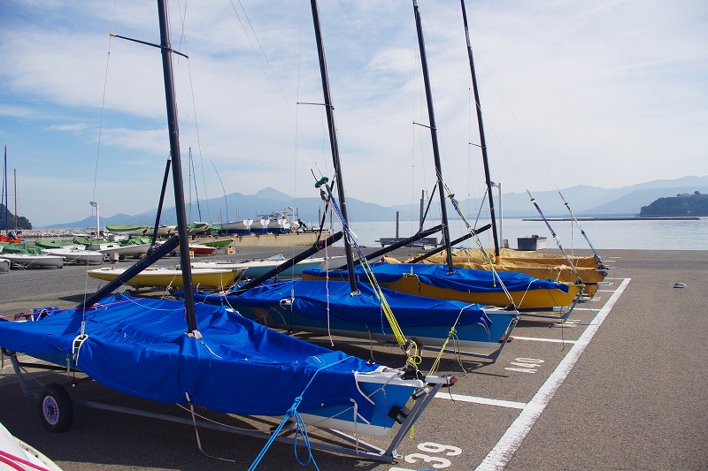 The Saga Prefecture Yacht Harbor is located in Karatsu City. In the boat park, there are several dinghies covered with blue covers.