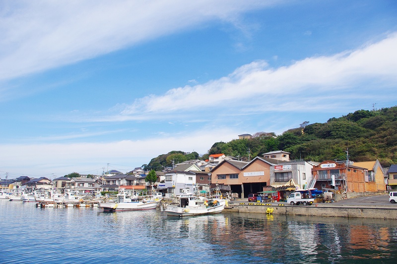 Yobuko fishing port. There are several fishing boats anchored in the harbor. Dried fish shops and houses are lined up.