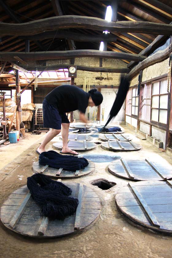 At the Indigo Dyeing Atelier Takeshi Yamamura, the indigo-dyed threads are being tapped into the hollows between the jars in order to better color them.