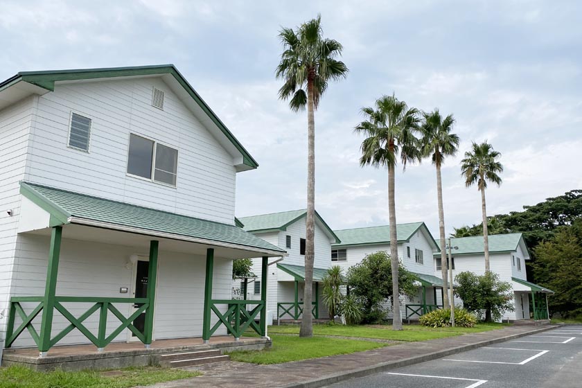 周防大島にある瀬戸内アロハリゾートグリーンステイながうらです。白壁に緑色の屋根の建物が4棟ならび、建物の前に高いパームツリーが4本立っています。