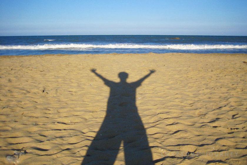 インドのチェンナイのビーチで、手を上げた影が砂浜に映っています
