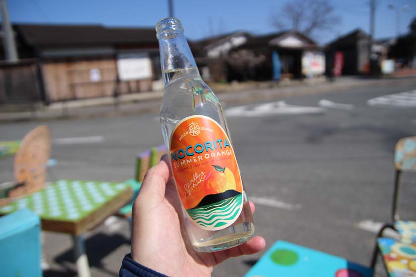 能古島オリジナルサイダー「ノコリータ NOCORITA」の瓶です。オレンジ色のラベルが瓶に貼られています。